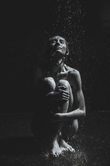 Fototapeta na wymiar A girl sits on the floor in the rain. Black and white photograph