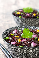 Black rice in a bowl and vegetables on wooden table

