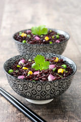 Black rice in a bowl and vegetables on wooden table

