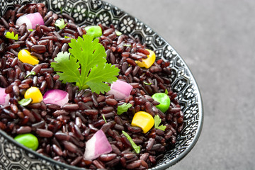 Black rice in a bowl and vegetables on black slate

