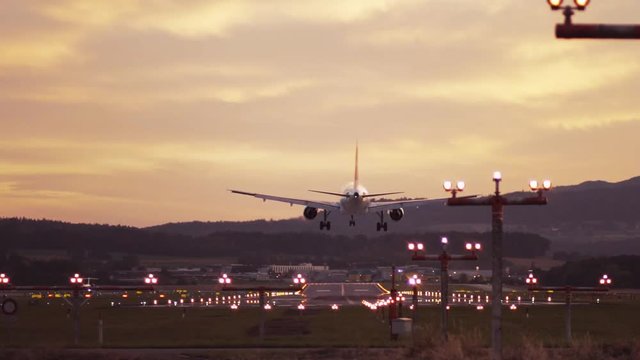 Evening sunset, big plane is landing. Airport lights are shining. No people around, contemporary atmosphere. Camera stabilizer shot, slow motion.