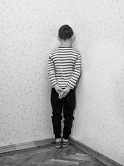 Monochrome of a lonely little boy who is standing corner of the room facing the wall