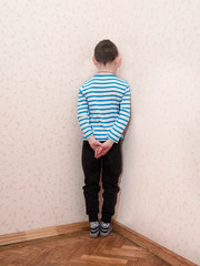 Toned image of a lonely little boy who is standing corner of the room facing the wall