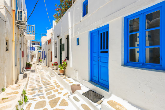 Fototapeta Typical white Greek houses with blue doors and windows on street of beautiful Mykonos town, Cyclades islands, Greece