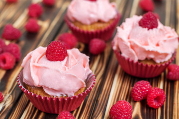 Delicious cupcakes with pink cream and fresh raspberries on a brown wooden table.