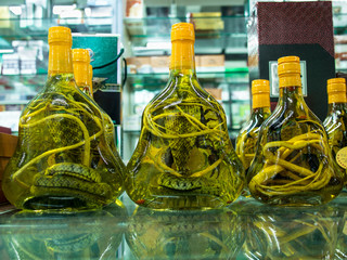 Glass jars with alcoholized snakes are on a glass table with reflection in Chinese traditional pharmacy boxes with soft background