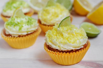 Lemon cupcakes with butter cream on white wooden table, slice of lemon and lime, selective focus, close up.