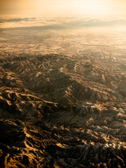 Toned image view from the window of an airplane to the Chinese mountains in winter on a background of sunset with clouds