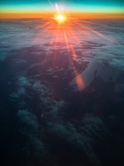 Toned image sunset above the clouds to the ground and lakes through an airplane window