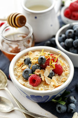 Porridge with addition fresh berry fruits, almond flakes, sesame seeds, lemon zest and honey. Delicious and healthy breakfast