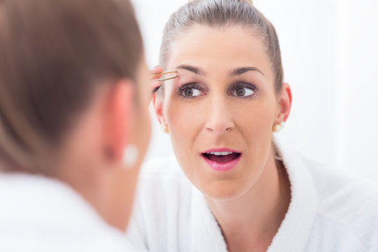 Frau im Badezimmer zupft sich die Augenbrauen