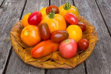 A few duferent colored tomatoes (red tomatoes,yellow tomatoes,colorful tomatoes) on carved wooden dish on wood background.