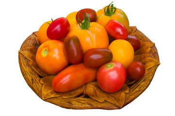 A few duferent colored tomatoes on carved wooden dish isolated on white background