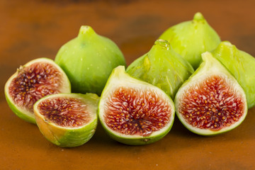 Several fresh figs with green skin and red flesh on a ceramics floor