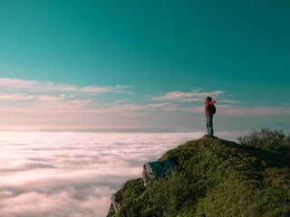 Toned image adult woman with a backpack stands on the edge of a cliff and looking at the sunrise against the blue sky and thick clouds floating down © atomfotolia