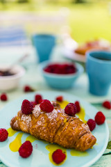 Delicious croissants and ripe raspberries on wooden table in the garden.