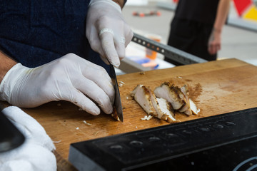 Closeup of the hands of a butcher cutting slices of meat off a l