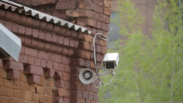 A CCTV camera on the side of the building it has a small megaphone on the side of the security camera