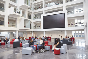 Students socialising under AV screen in atrium at university