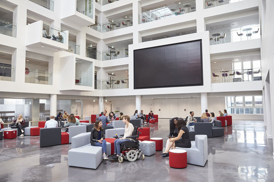 Students socialising under AV screen in atrium at university