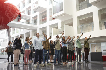 Students in a university atrium taking photos with phones