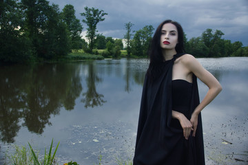 Beautiful brunette woman in black dress and black cloak