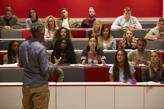 Back View Of Man Presenting To Students At A Lecture Theatre