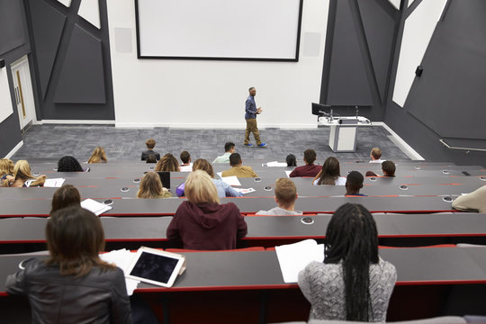 Man lectures students in lecture theatre, back row seat POV