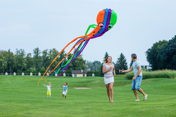 Happy family flying kite together on green field