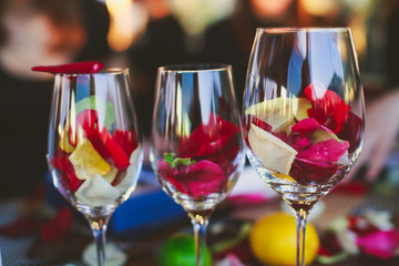 Beautiful glass with rose leafs, rose-petal, rose petals on a romantic date with wine, candles in candlelight and with celebrating couple on the background, interior for a romantic date diner 