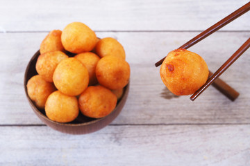 Top view of a bowl of deep fried sweet potato balls on a wooden table.