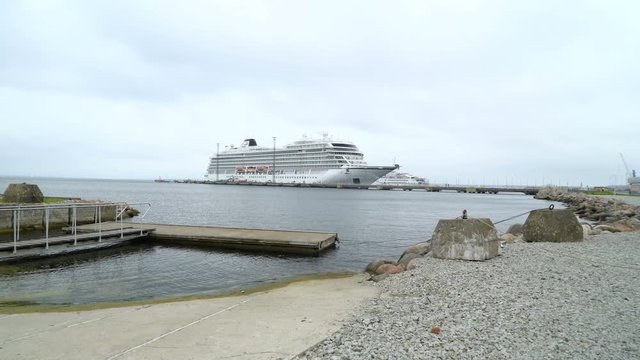The port with rocky shore of the sea and a docking cruise ship on the far