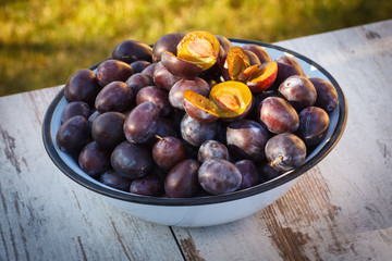 Heap of plums in metal bowl on wooden table in garden on sunny day