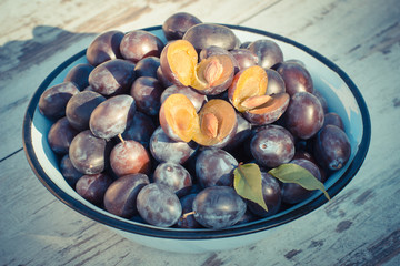 Vintage photo, Heap of plums in metal bowl on wooden table in garden on sunny day