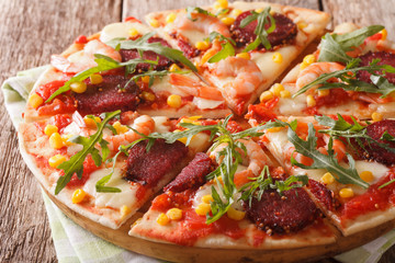 Hot pizza with shrimp, salami, cheese and arugula close-up on a wooden. horizontal
