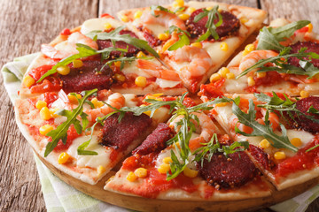 Hot pizza with shrimp, salami, cheese and arugula close-up on a wooden. horizontal
