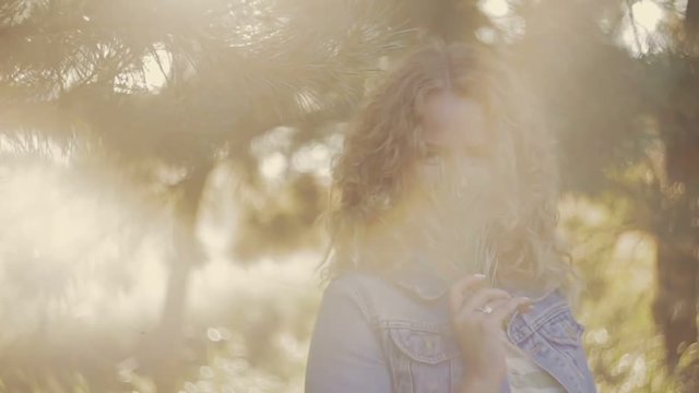 Young European woman is standing under the tree, smiling and covering her face with pine’s twig. Warm atmosphere. Outside shooting, female portrait. Close up view, stabilizer shot.