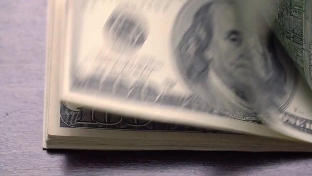 A large stack of hundred dollar bills on a table gradually blows away to nothing.