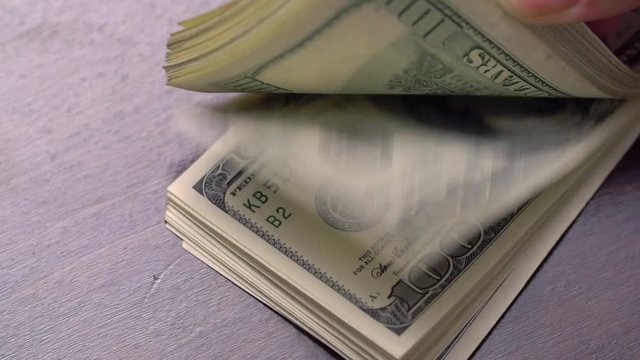 A large stack of hundred dollar bills on a table gradually blows away to nothing.