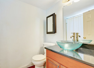 White interior of bathroom with wooden vanity and glass sink.