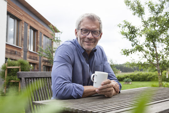 Portrait of confident mature man with cup at garden table