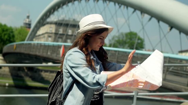 Pretty girl standing next to the river and reading a map
