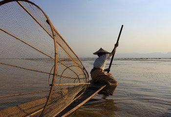 Burmese fisherman on bamboo boat catching fish in traditional way with handmade net. Inle lake, Myanmar (Burma) - 119125042