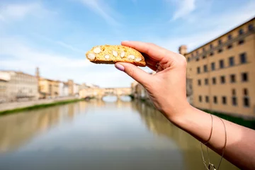 Fotobehang Female hands holding cantuccini cookie on the river background in Florence city in Italy. Cantuccini is traditional italian almond biscuits © rh2010