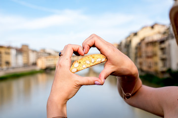 Female hands holding cantuccini cookie on the river background in Florence city in Italy....