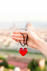 Fototapeta premium Female hand holding pendant in form of the heart on the old town background in Florence