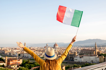 Young female traveler waving italian flag on the old town background in Florence in the morning. Promoting tourism in Italy. Back view with copy space