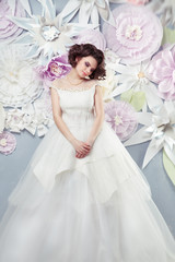 Beautiful young bride in an elegant dress on a background of a large paper flowers