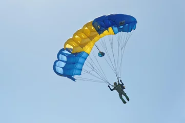 Fototapeten Paraglider flying on colorful parachute in blue clear sky at a bright sunny summer day. Active lifestyle, extreme hobbies © sergbob