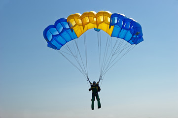 Paraglider flying on colorful parachute in blue clear sky at a bright sunny summer day. Active lifestyle, extreme hobbies